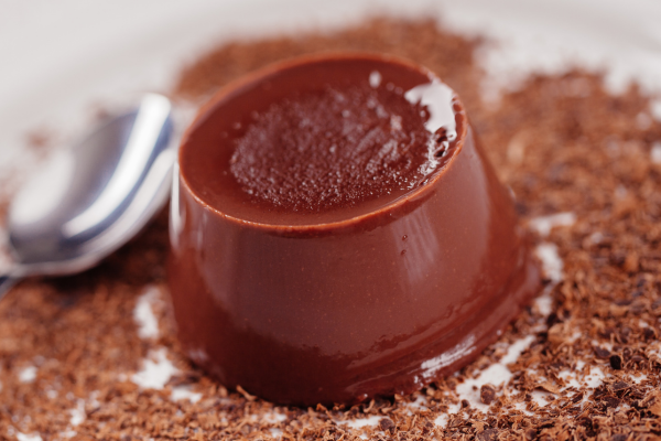 pudim de chocolate e uma olher ao lado com farelos de chocolate em volta